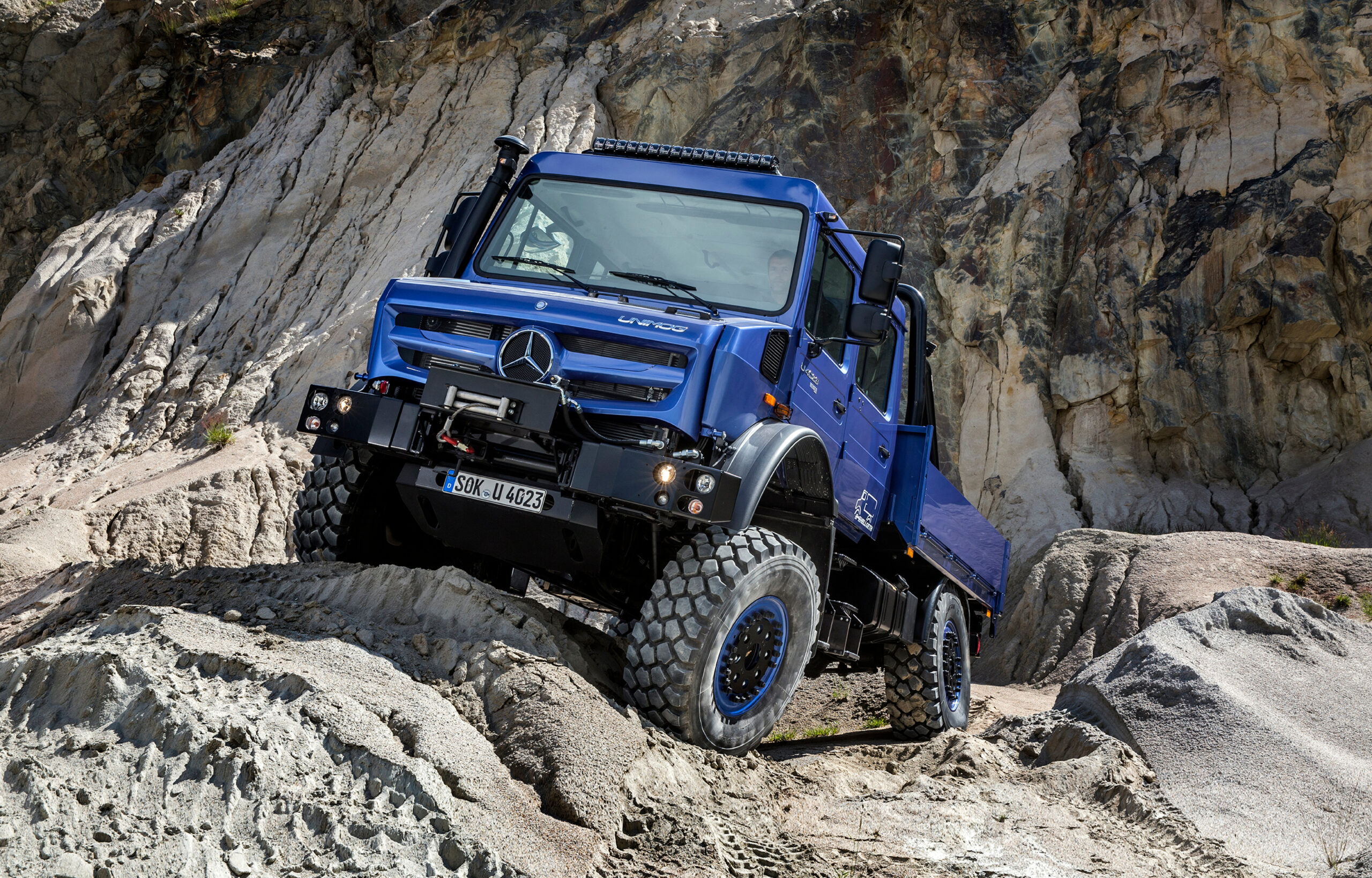 Auf dem Bild ist ein blauer Unimog auf einem Kieshügel zu sehen