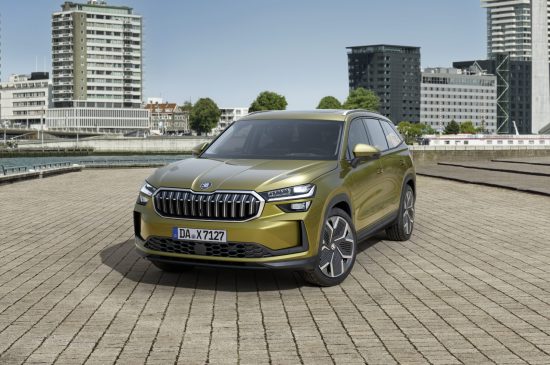 Auf dem Bild ist ein grüner Skoda Kodiaq zu sehen. Im Hintergrund sieht man mehrere Hochhäuser und ein kleiner Fluss.